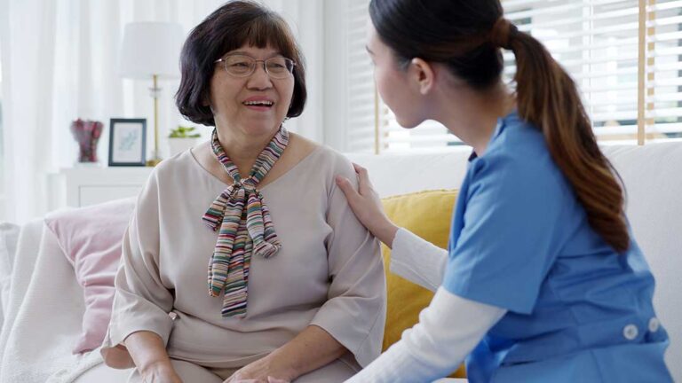 Older adults talking with staff in a cozy assisted living common area, with personal belongings nearby.