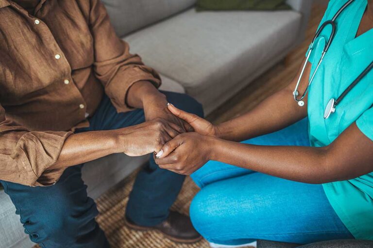 Family members talk with an older adult in a bright assisted living room beside a small table and family photos.